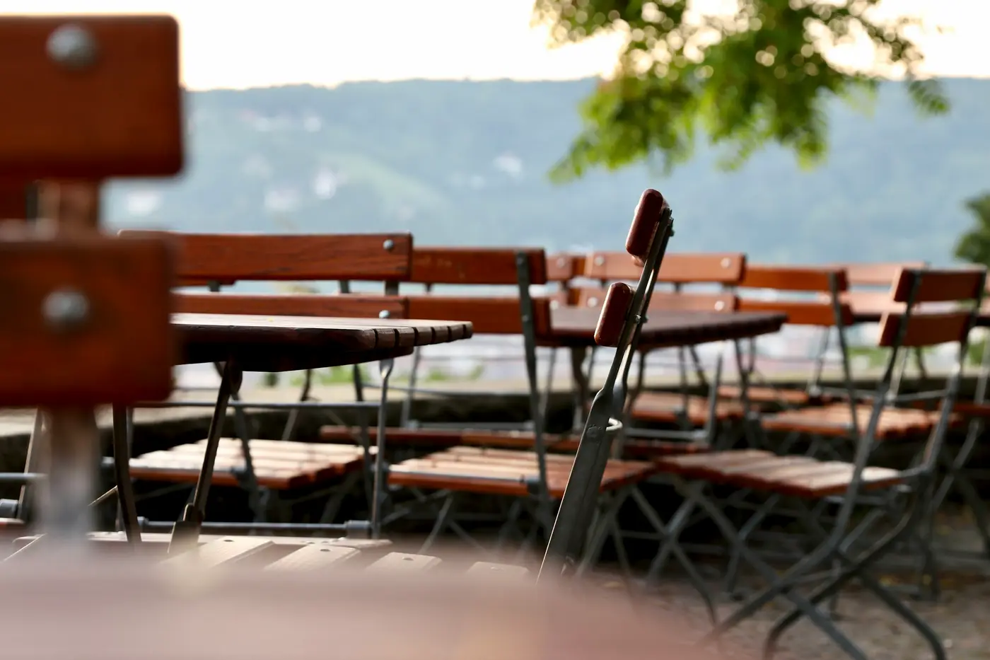 Holzbänke und Klappstühle eines Biergartens am Abend, im Hintergrund Hügel