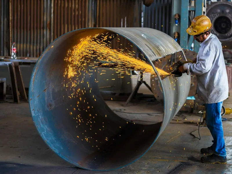 Metallbauer schleift in einer Werkstatt ein großes Stahlrohr, Funken fliegen