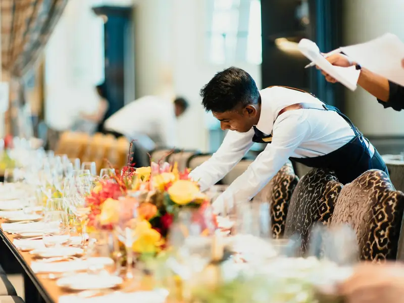 Kellner deckt eine lange Tafel mit Blumen und Gläsern ein